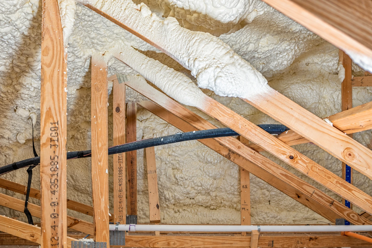 White closed-cell spray foam fills the spaces around wooden rafters and beams beneath a roof.