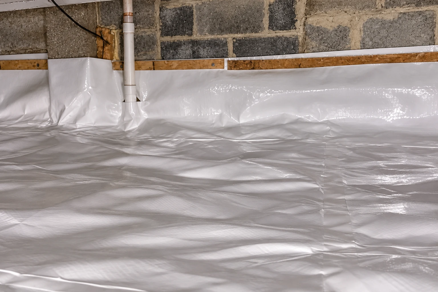 A crawl space floor and lower block walls are covered with a glossy white vapor barrier.
